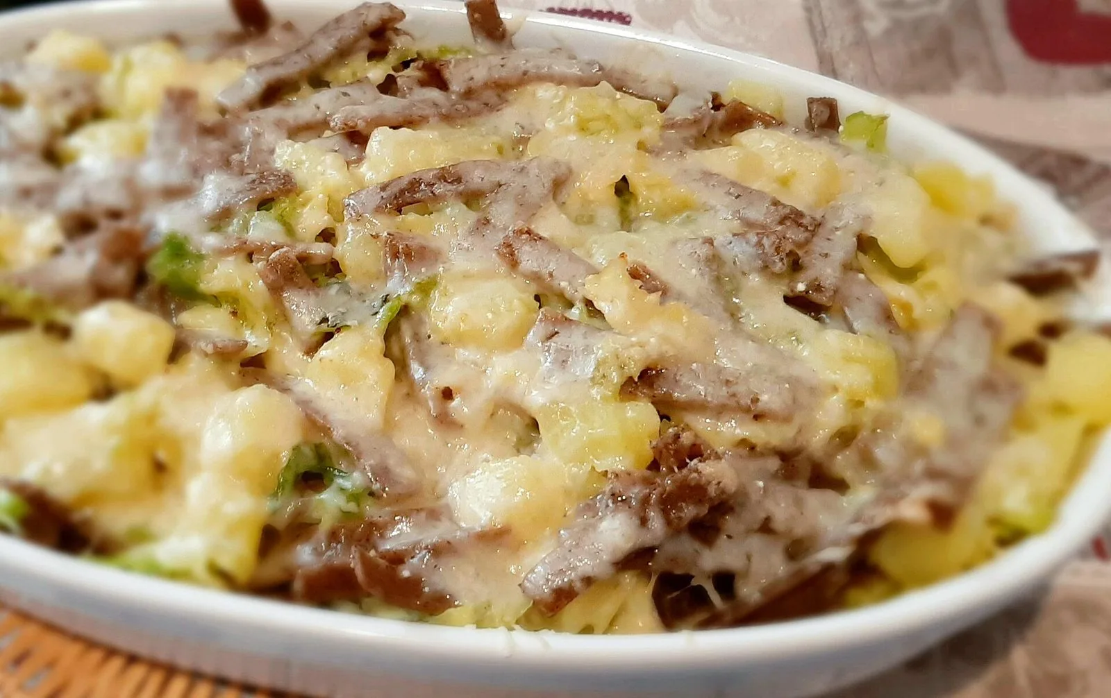 Una pirofila bianca colma di pizzoccheri della Valtellina: tagliatelle scure di grano saraceno con patate, verza e formaggio fuso, su una tovaglia chiara